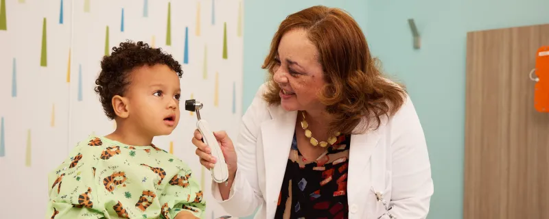 A doctor in a lab coat checks the ears of a young patient at Children's National Hospital.
