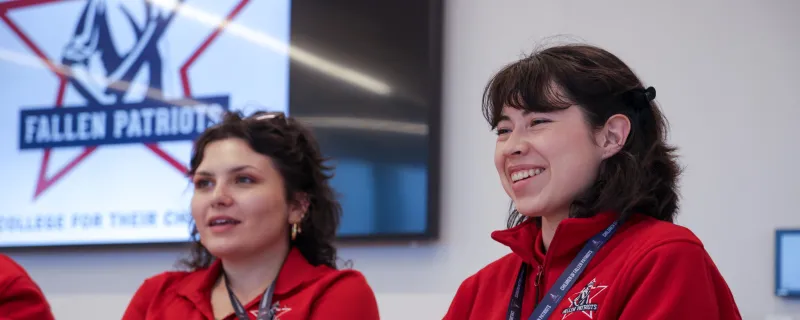 Two Children of Fallen Patriots staff members laugh and smile as they greet guests at a gathering.