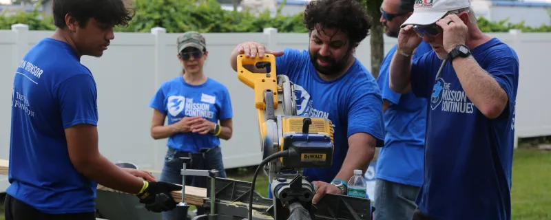 Volunteers from The Mission Continues operate a table saw during a service project.
