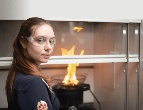 Raquel Hakes Weston-Dawkes stands in front of a flame in a science lab