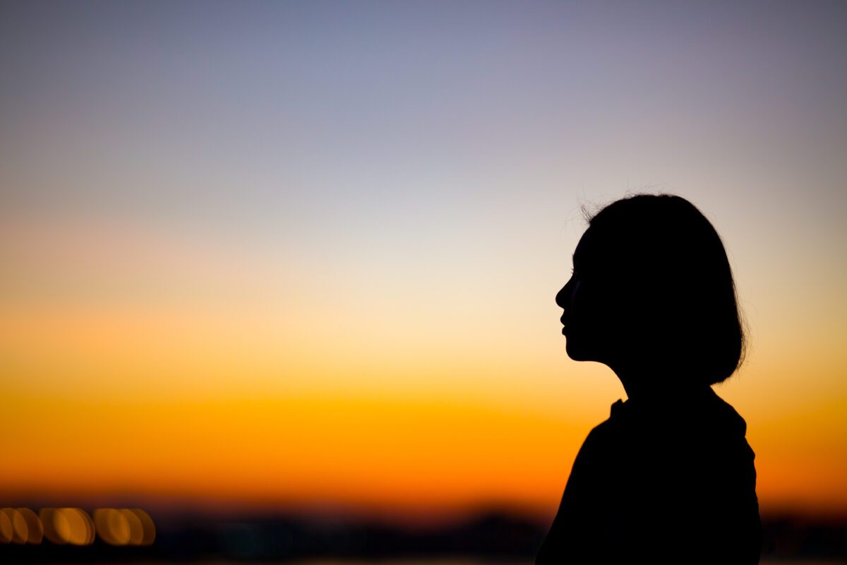 Woman stands with sunsetting behind her